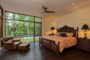 A bedroom with a bed, chair and pool in the background.