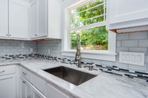 A kitchen with white cabinets and marble counter tops.