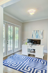 A white desk with two monitors and a blue rug.