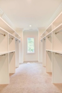 A large walk in closet with many white shelves.