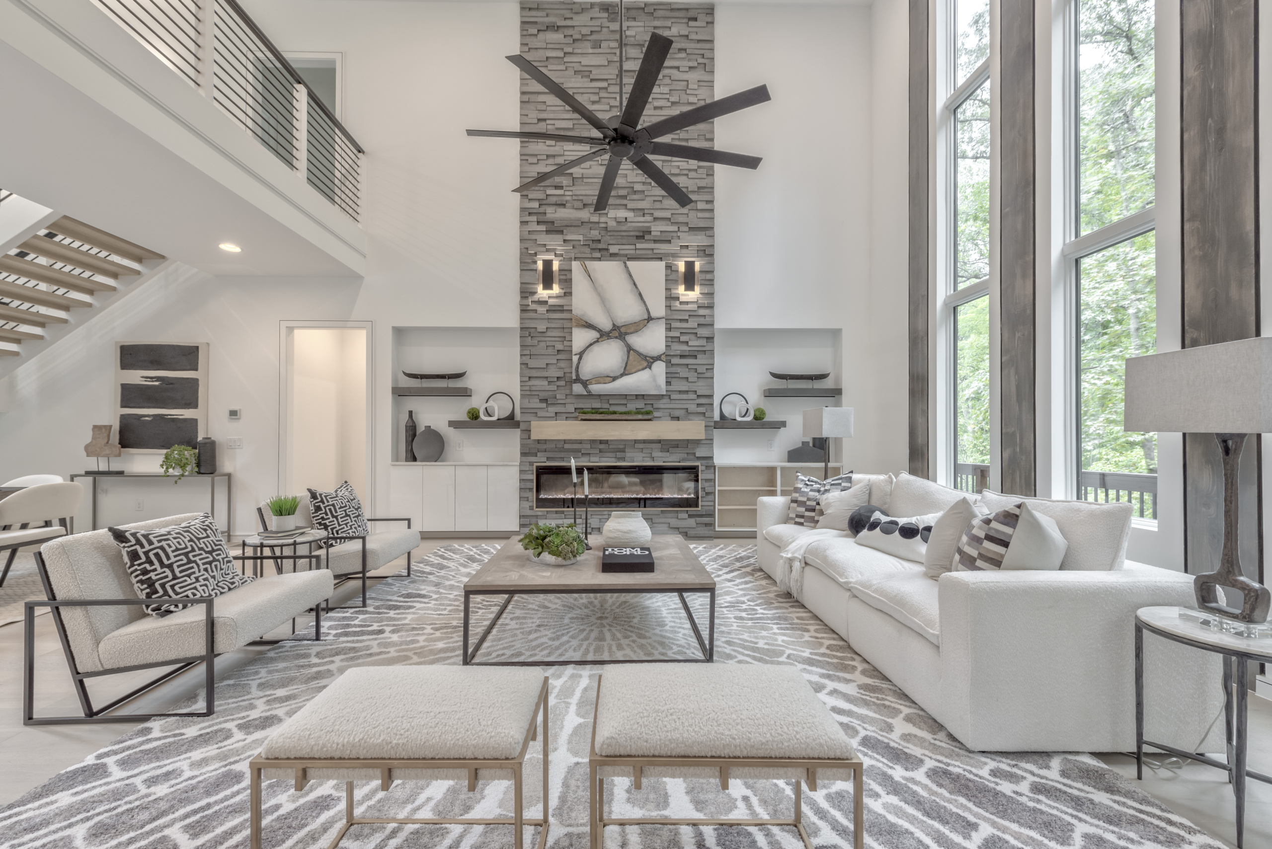 Modern gray and white living room with floor to ceiling windows, high ceilings, and inset fireplace with stone wall detail and floating staircase with open catwalk