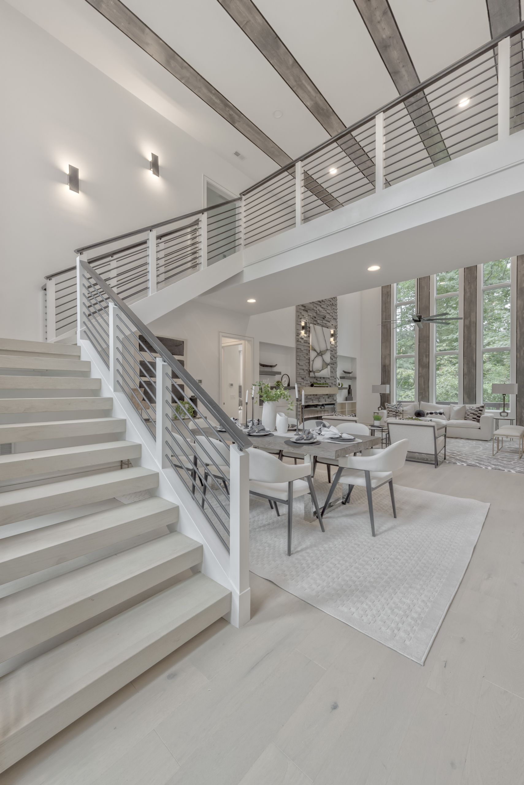 Floating staircase with aluminum railings, floor to ceiling windows and wall sconce lighting and open catwalk with open dining room and living room with tall ceilings