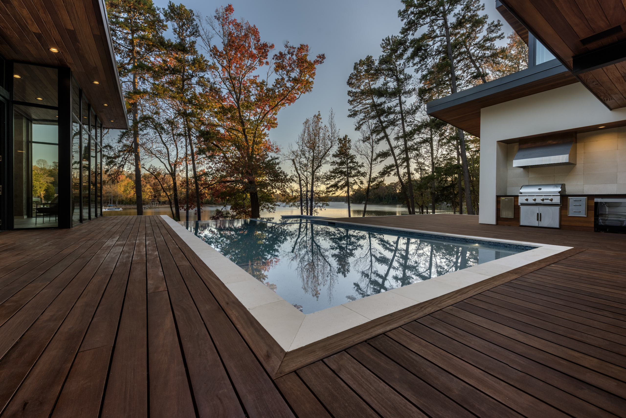 A pool with wooden deck and trees in the background.