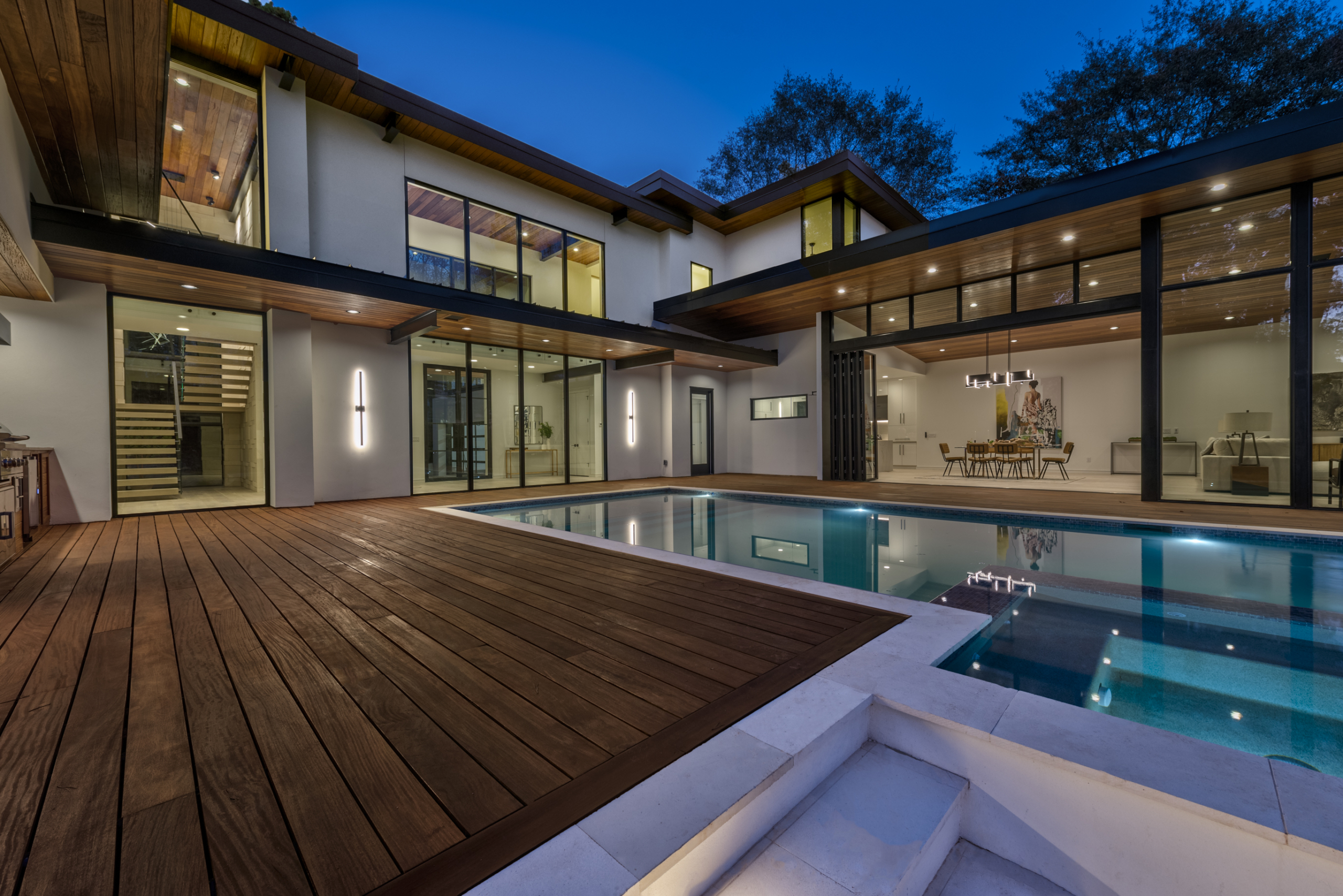 During night Cumaru wood decking and custom infinity pool outside house with folding glass doors