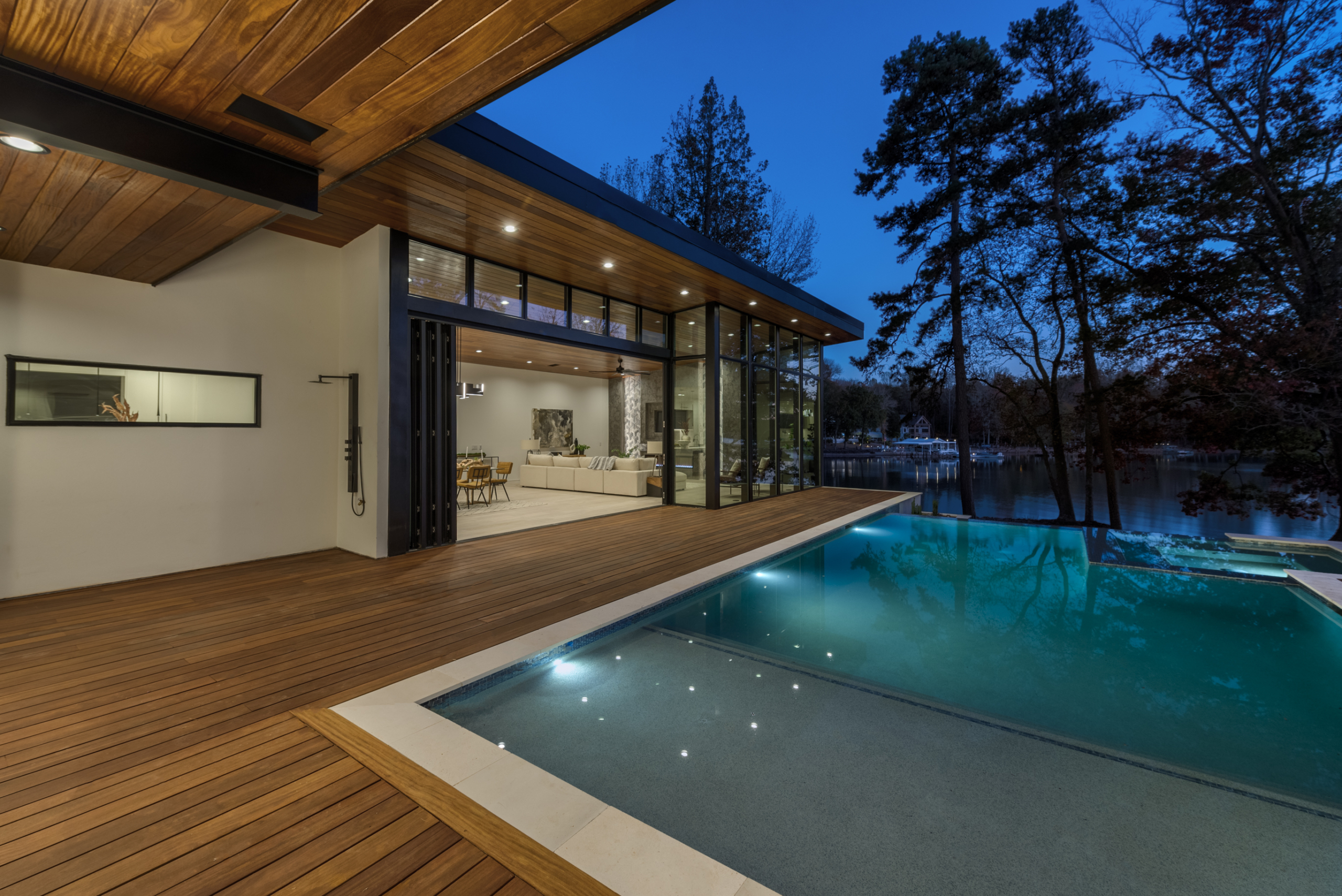 During night House with folding glass door wall and Cumaru wood deck and custom heated pool with infinity edge, oversized spa, tanning ledge and LED lighting package, pebble plaster finish and limestone coping