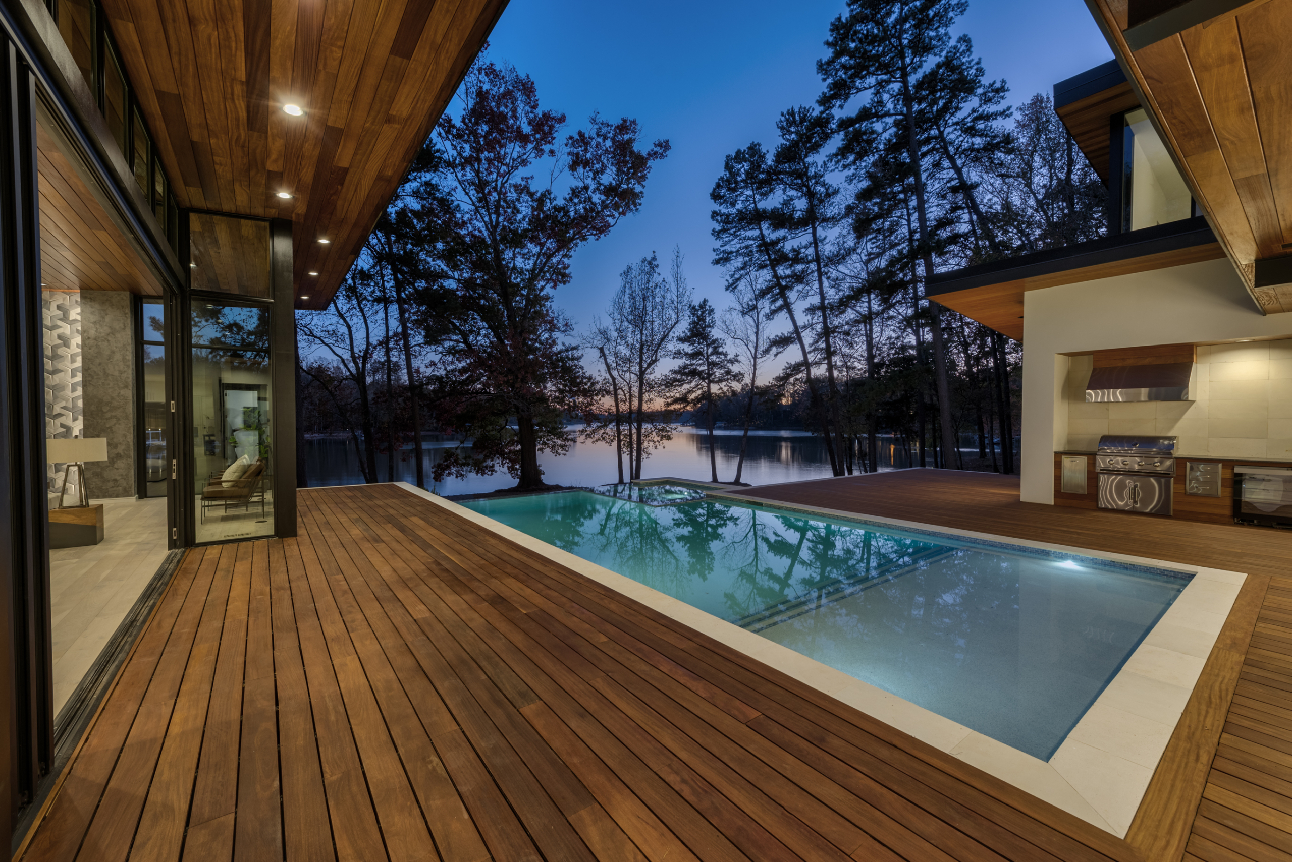 During night Cumaru wood deck and custom heated pool with infinity edge, oversized spa, tanning ledge and LED lighting package, pebble plaster finish and limestone coping