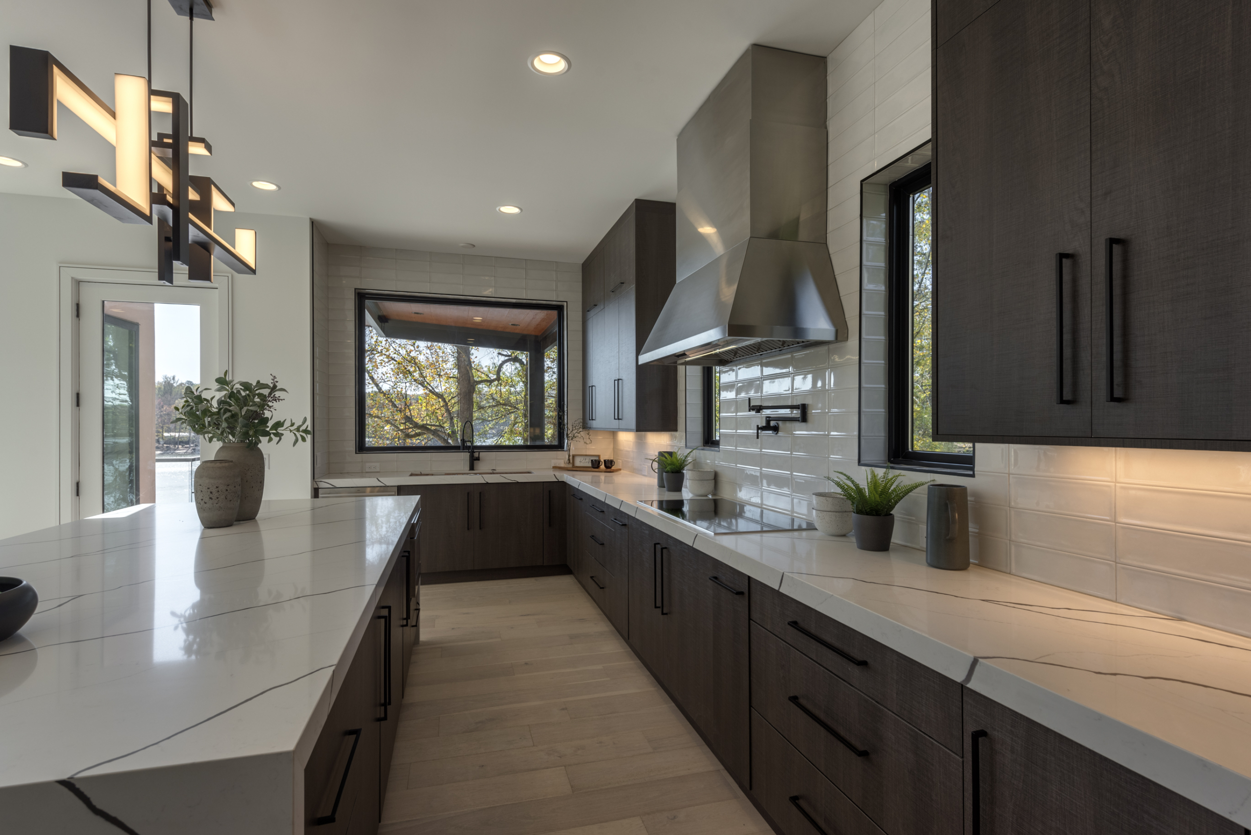 Kitchen has professional Monogram appliances with modern dark wood European cabinetry and a massive 10’ long x 5’ wide waterfall island. Includes a 42” Miele induction cooktop and pot filler, and subway tile white backsplash, waterfall island, white marble thick countertops