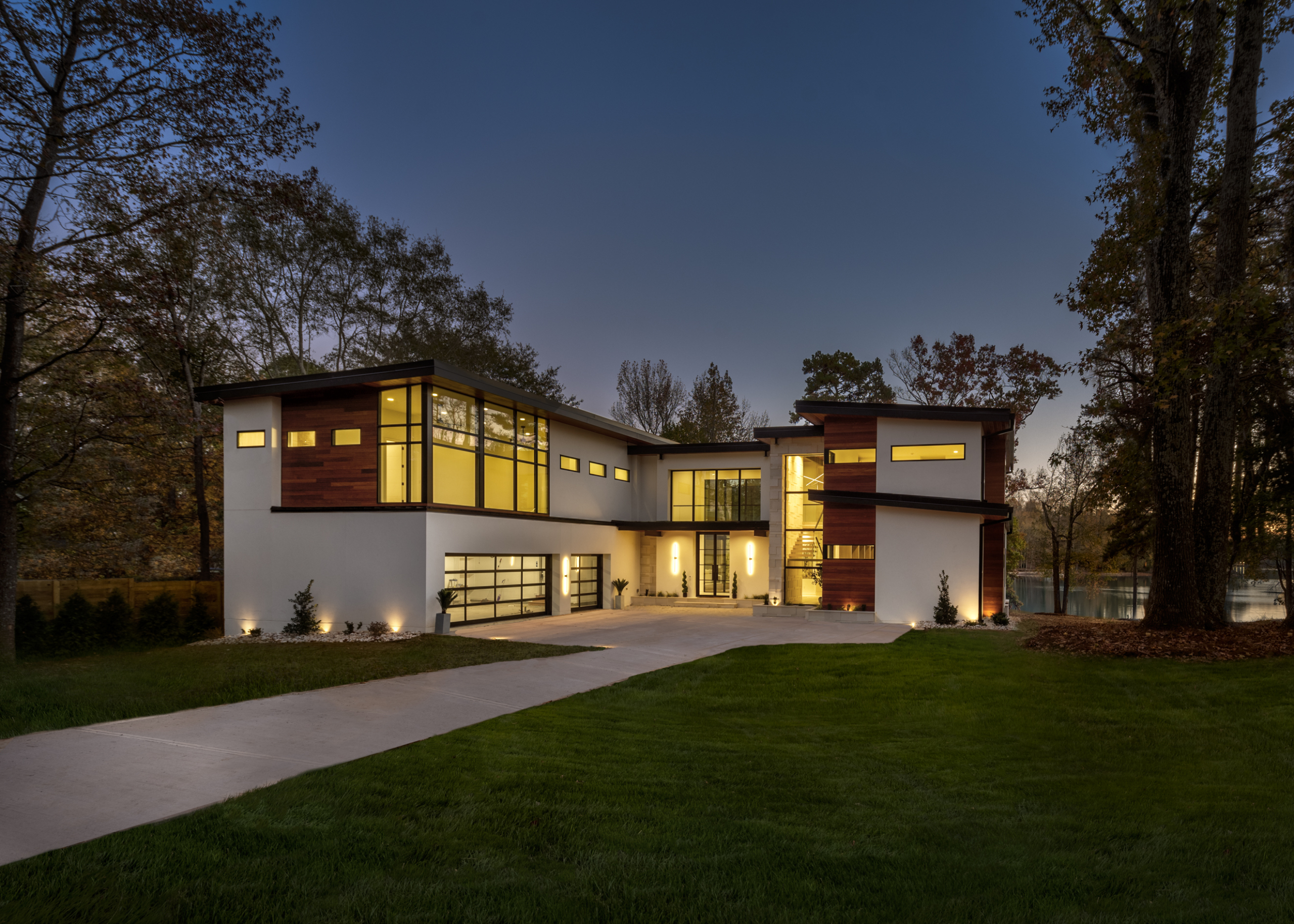 Modern contemporary home at night with white hard coat stucco walls, cumaru wood, floor to ceiling windows