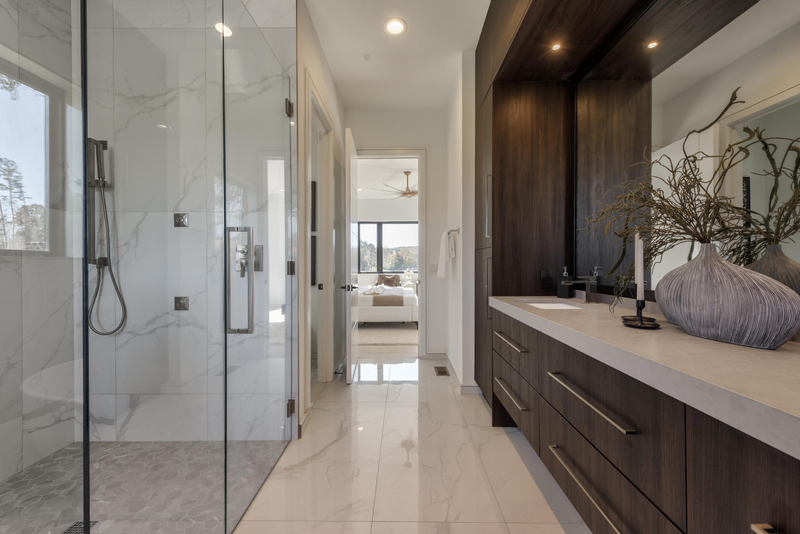 Modern bedroom bathroom with custom large floor to ceiling dark wood double vanity leading into bedroom