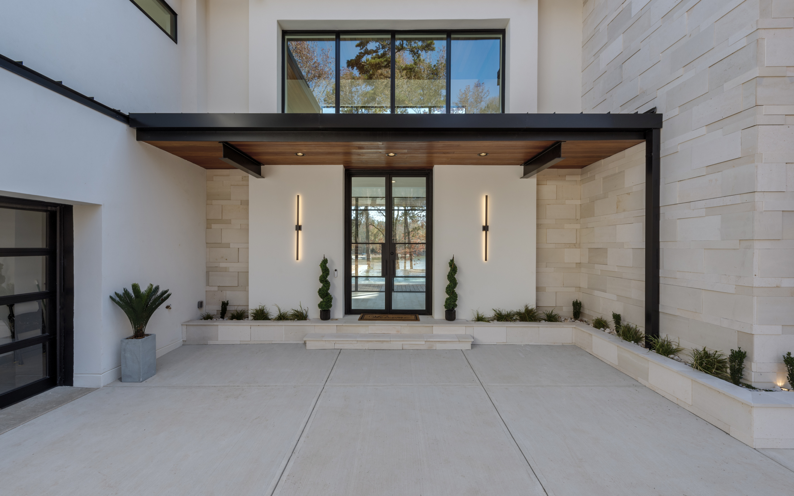 Modern contemporary home with 6’ wide x 10’ tall wrought iron and glass French front door, white hard coat stucco walls, and Imported, custom-cut-pattern White Palimanan Limestone from Bali, Indonesia