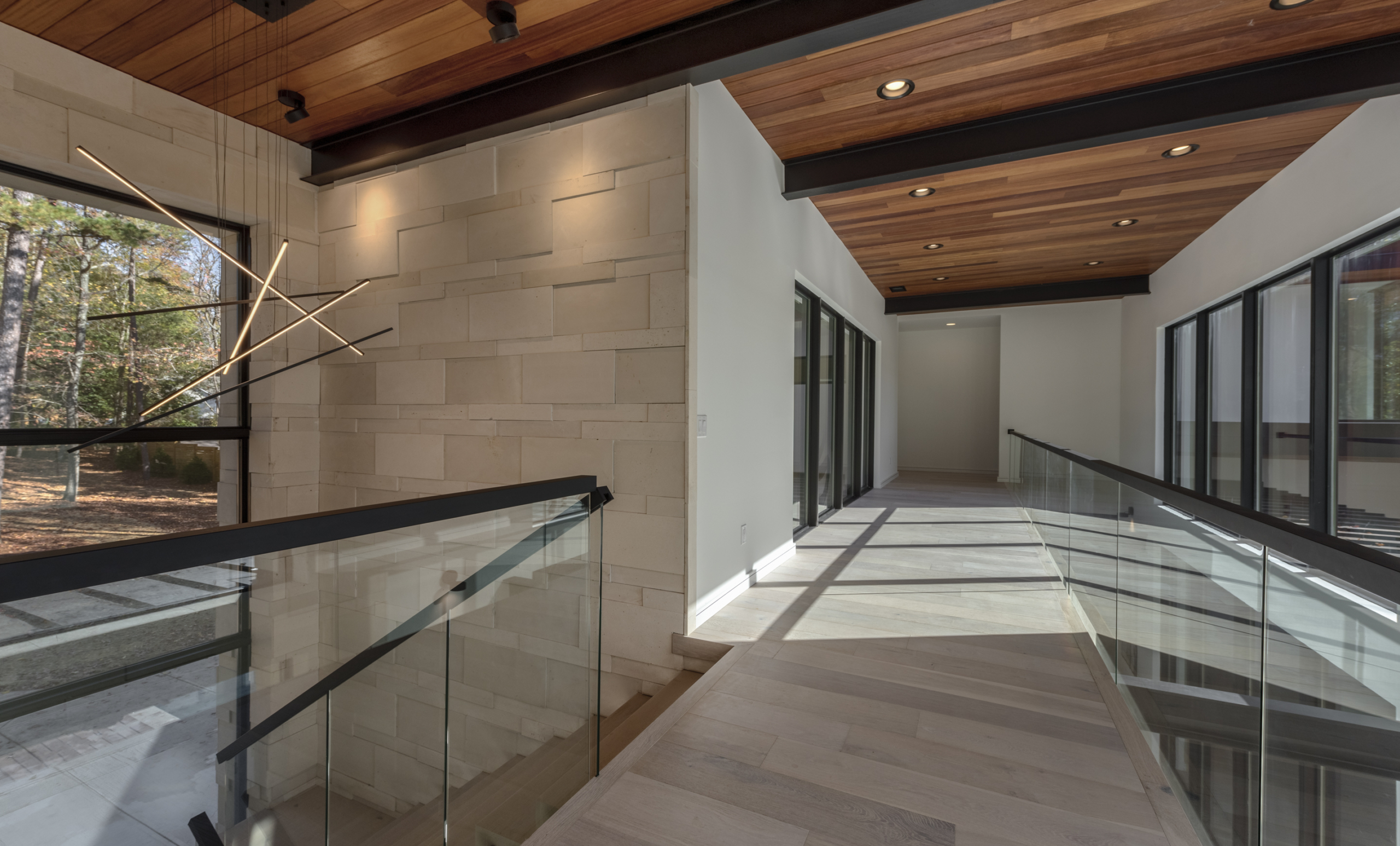Hallway with cumaru ceiling and all glass railing and custom palimanan limestone wall
