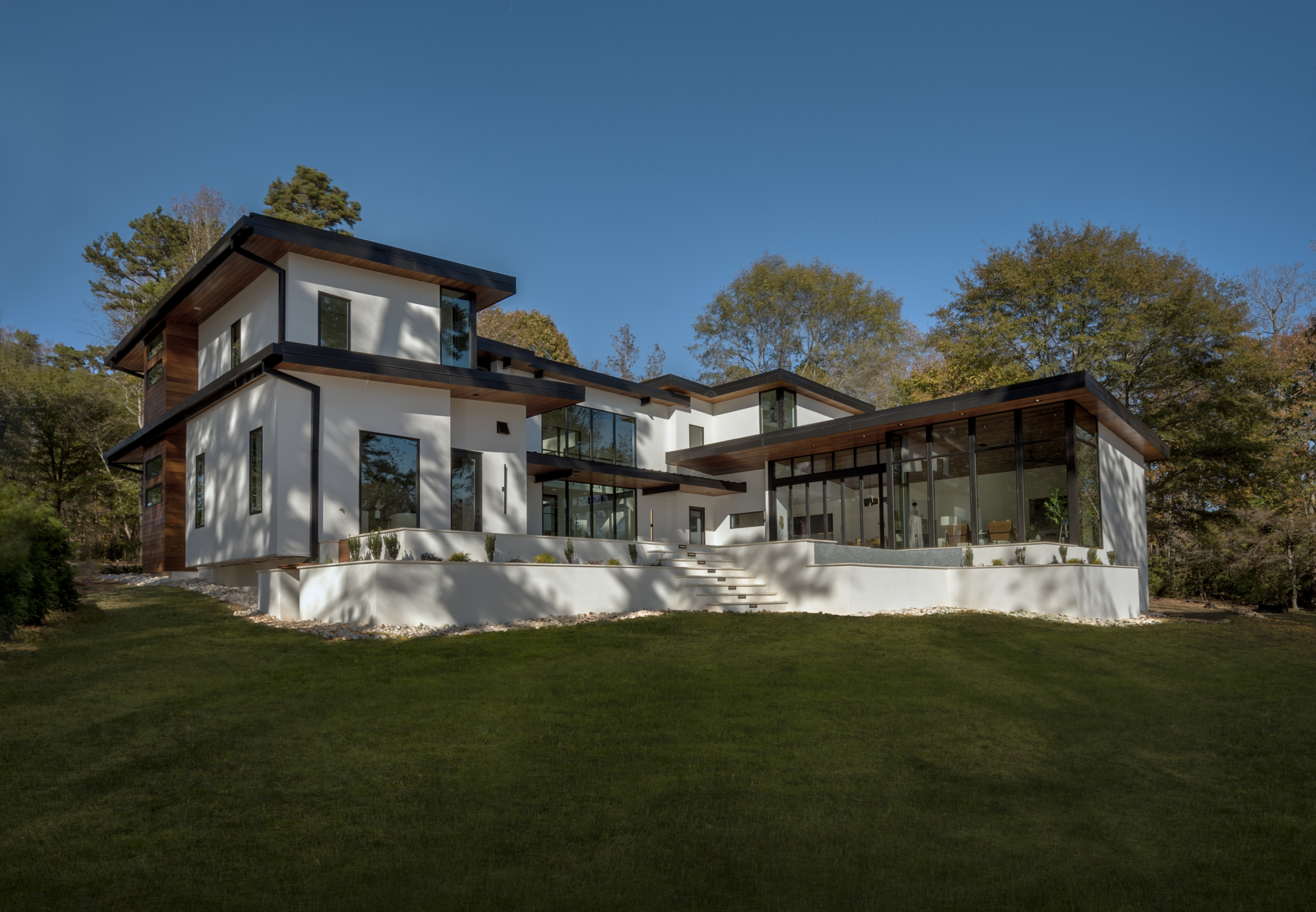 Modern contemporary home with floor to ceiling windows, Permanent black standing-seam metal roof, imported exotic cumaru wood, and hard coat white stucco during day