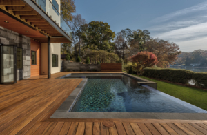A pool with a wooden deck and a house in the background.