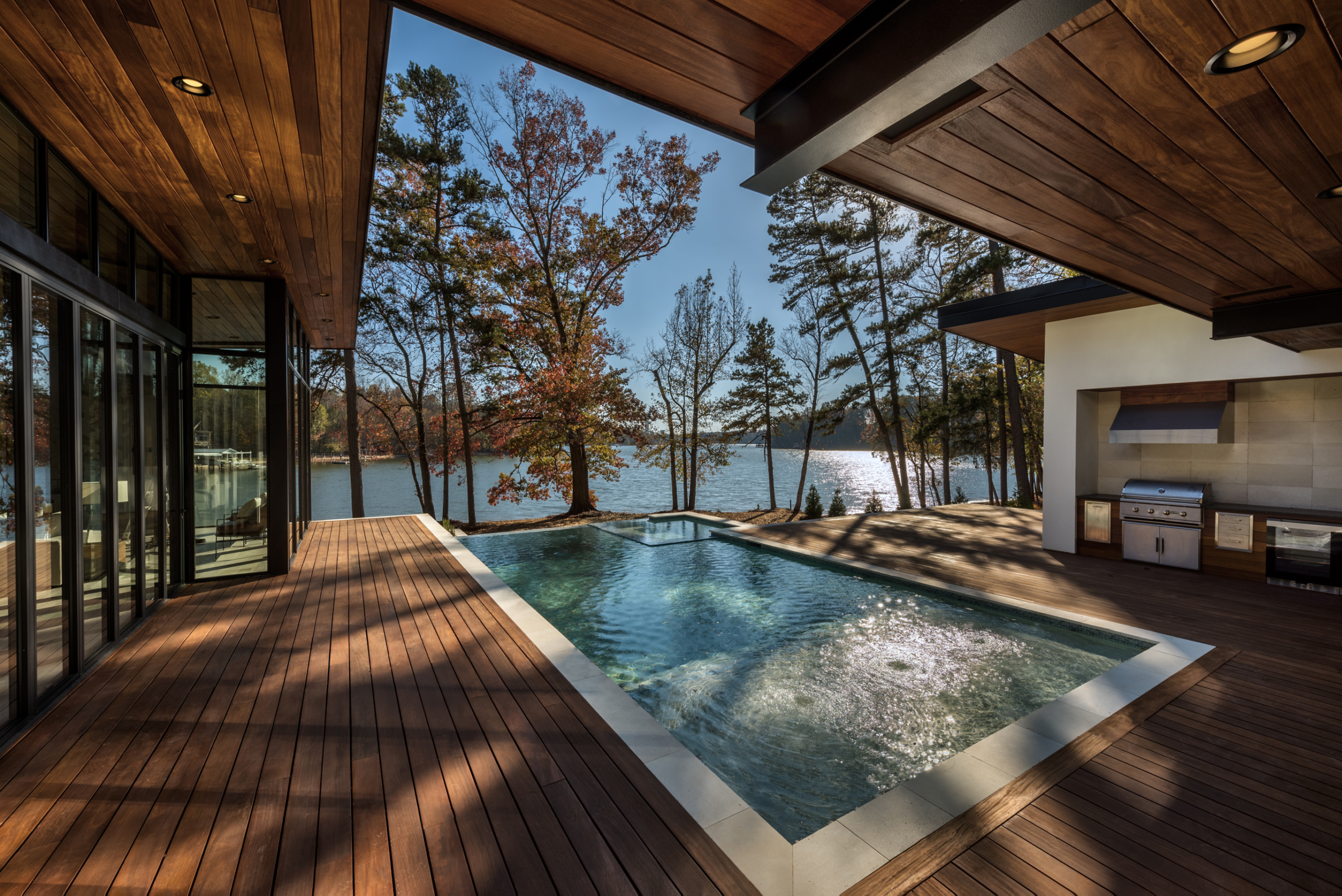 Cumaru wood deck and custom heated pool with infinity edge, oversized spa, tanning ledge and LED lighting package, pebble plaster finish, outdoor kitchen and limestone coping during day
