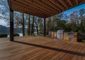 A large wooden deck with an outdoor grill and a lake view.