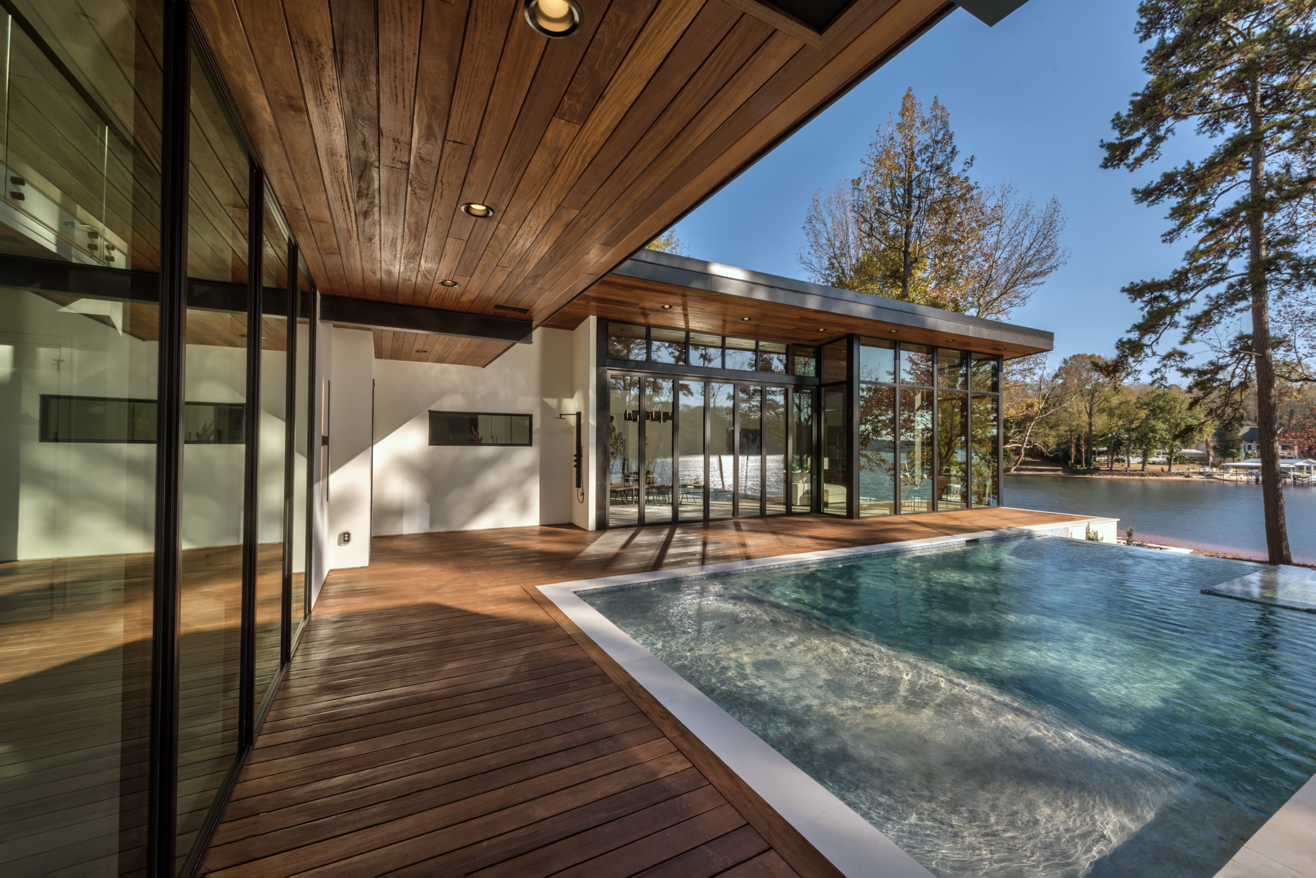 House with Palisades aluminum glass folding door open to Cumaru wood deck and custom heated pool with infinity edge, oversized spa, tanning ledge and LED lighting package, pebble plaster finish and limestone coping during day