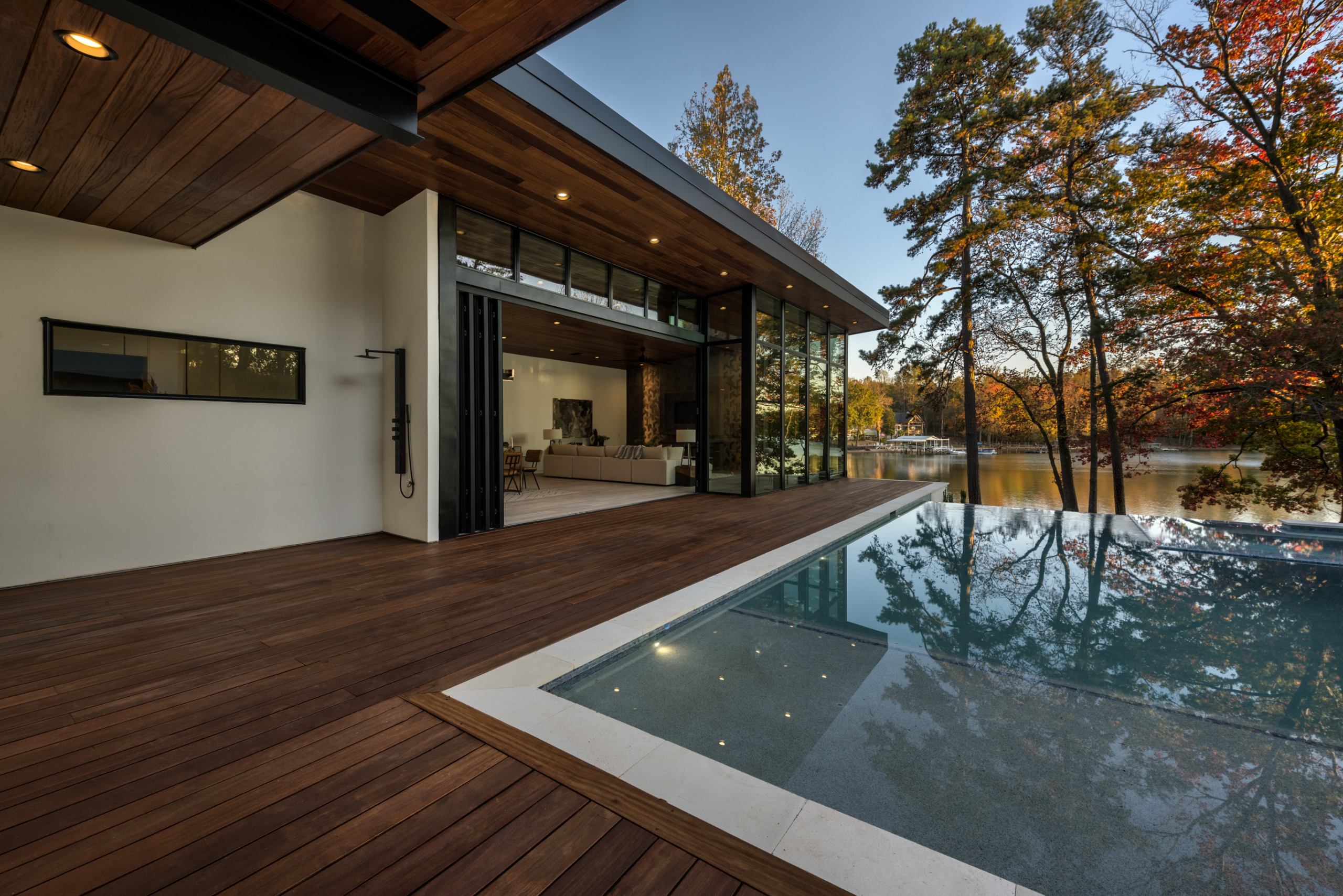 House with Palisades aluminum glass folding door open to Cumaru wood deck and custom heated pool with infinity edge, oversized spa, tanning ledge and LED lighting package, pebble plaster finish and limestone coping during day