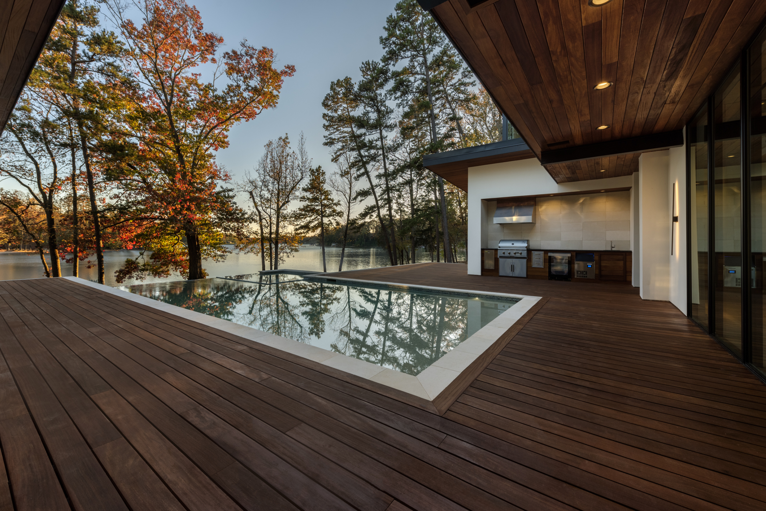 Cumaru wood deck and custom heated pool with infinity edge, oversized spa, tanning ledge and LED lighting package, outdoor kitchen, pebble plaster finish and limestone coping during day
