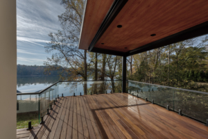 A wooden deck with glass railing and a lake view.