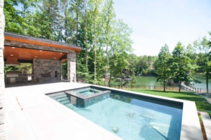 A pool with a stone wall and a large concrete deck.