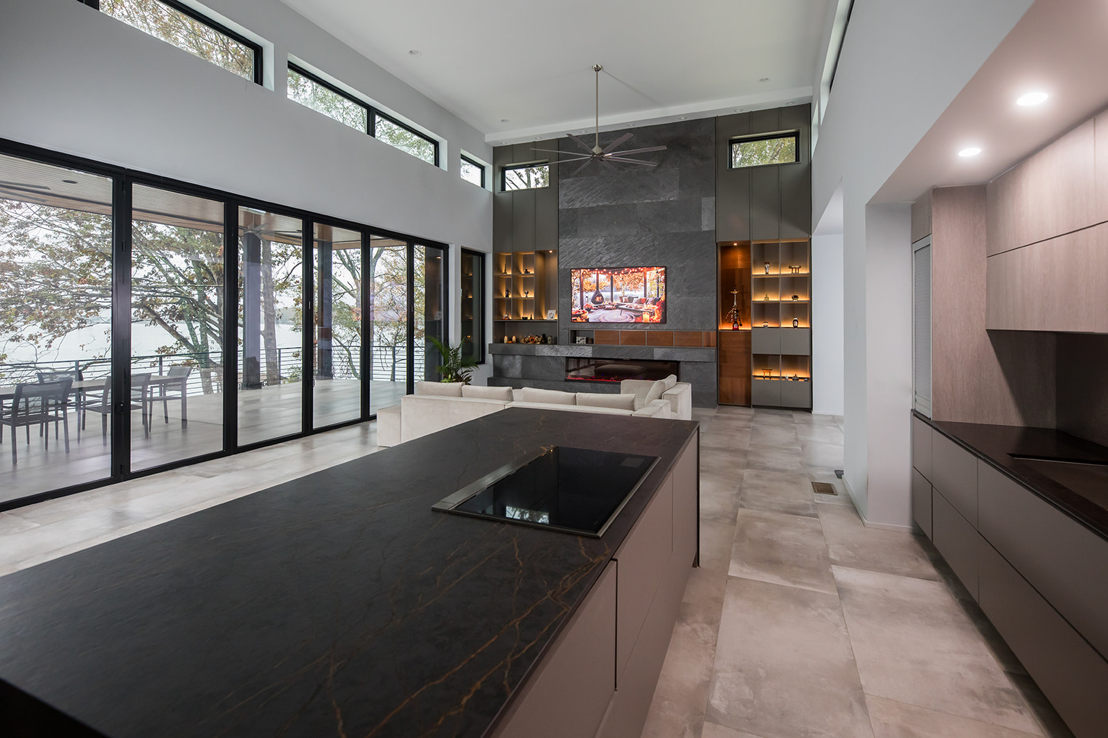 Modern gray slate living room with open floor plan kitchen with electric fire place, natural light, and folding glass doors.