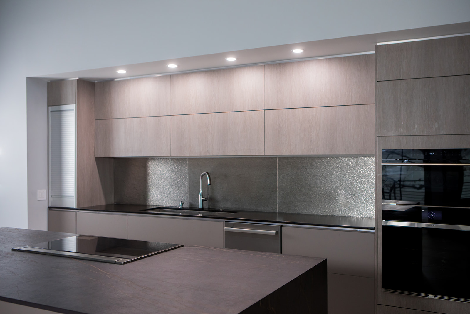 Modern gray slate minimalist kitchen with, stainless steel hardware, electric flat stove, and metallic backsplash