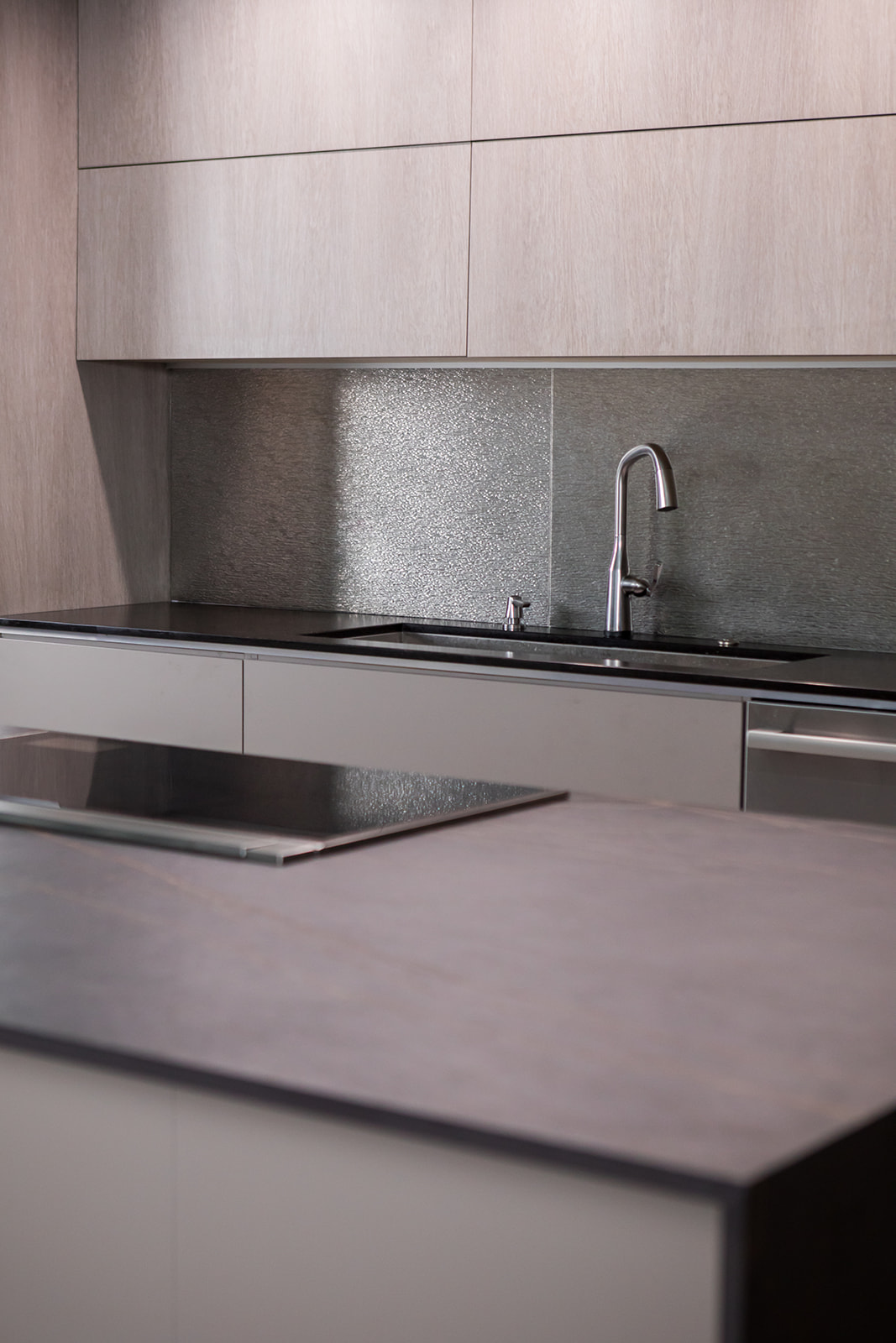 Modern gray slate minimalist kitchen with, stainless steel hardware, electric flat stove, and metallic backsplash