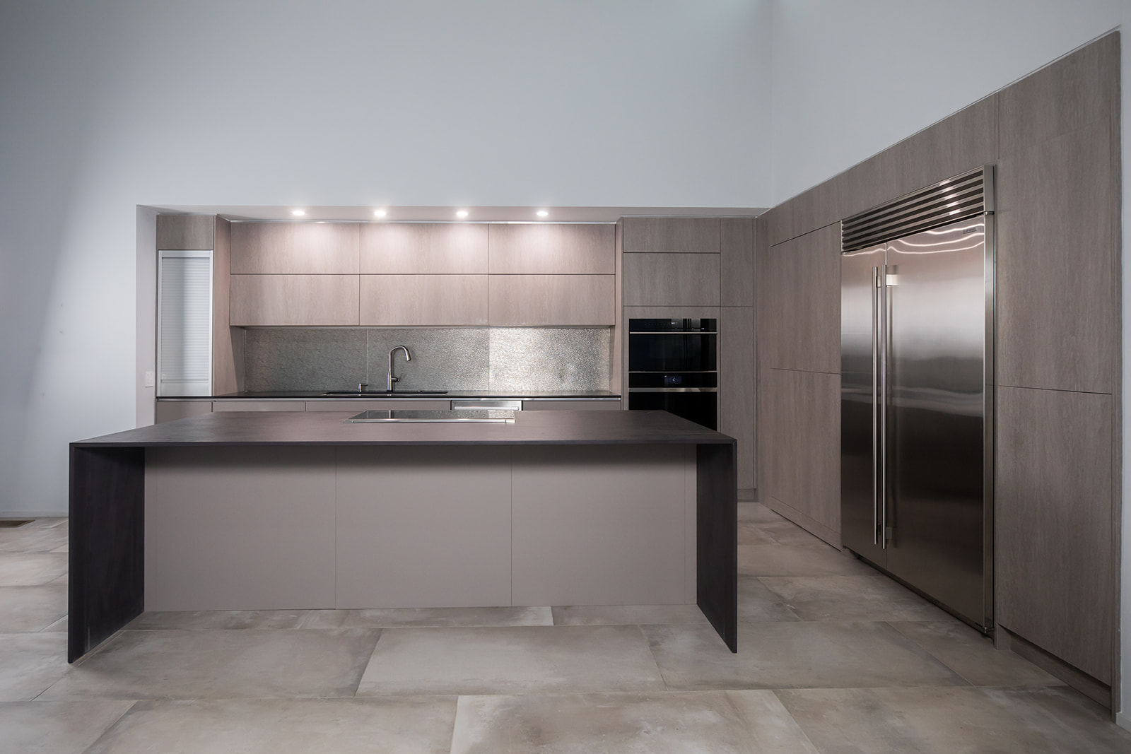 Modern gray slate minimalist kitchen with waterfall countertop, stainless steel hardware, electric flat stove, and metallic backsplash