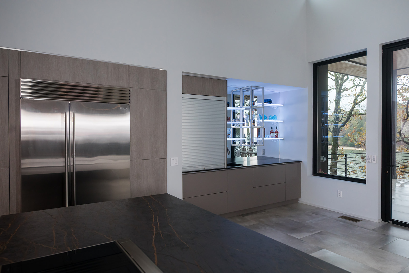 Modern gray slate minimalist kitchen with waterfall countertop, stainless steel hardware, electric flat stove, and bar display, and natural light