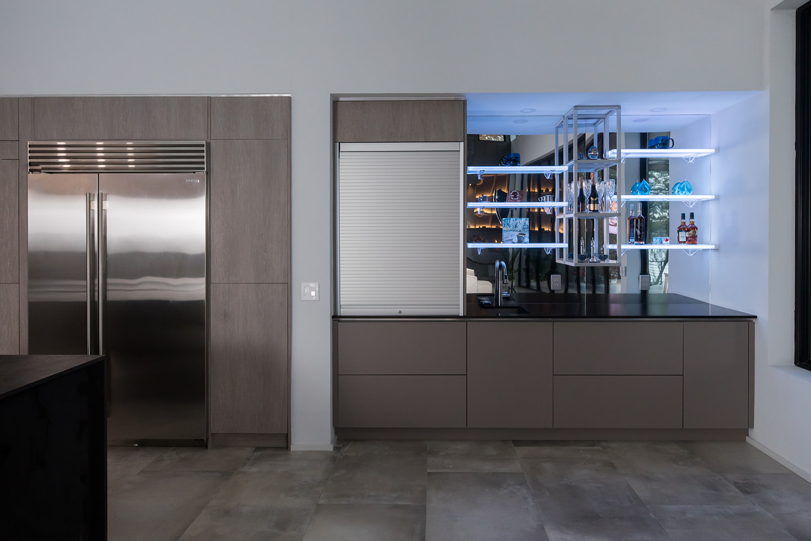 Modern gray slate minimalist kitchen with waterfall countertop, stainless steel hardware, electric flat stove, and bar display, and natural light