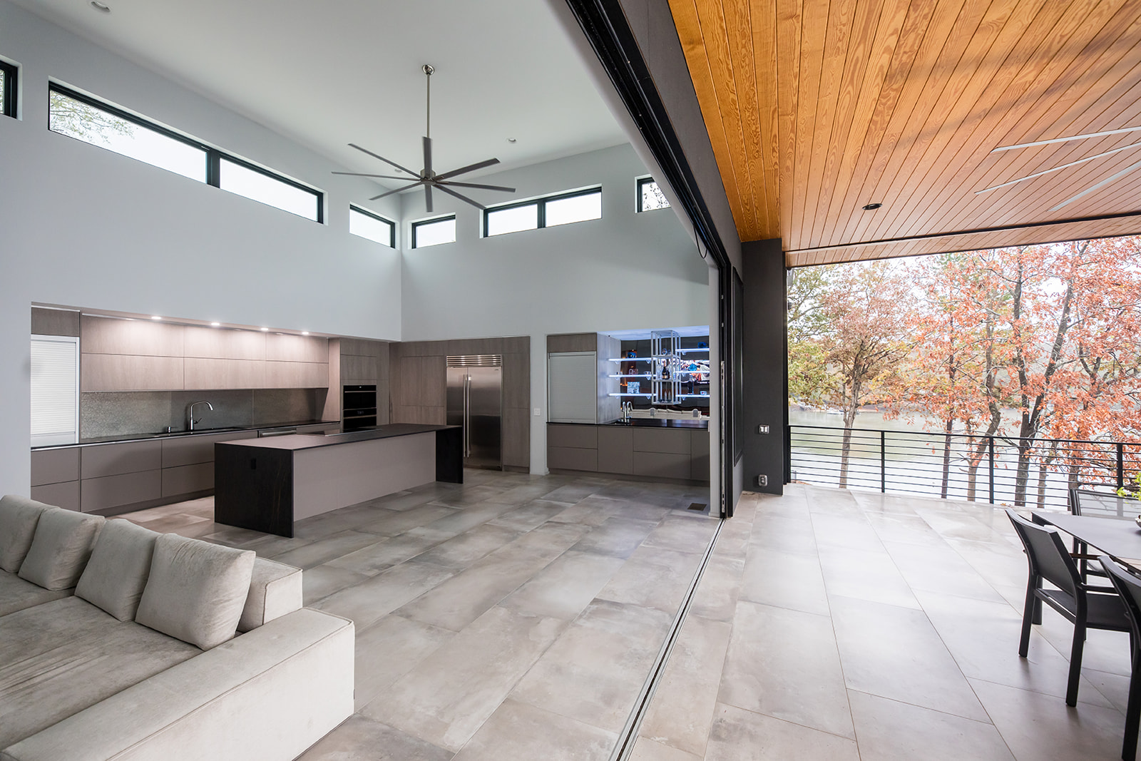 Modern living room and open floor plan gray kitchen opens to outdoor dining area with folding french glass doors