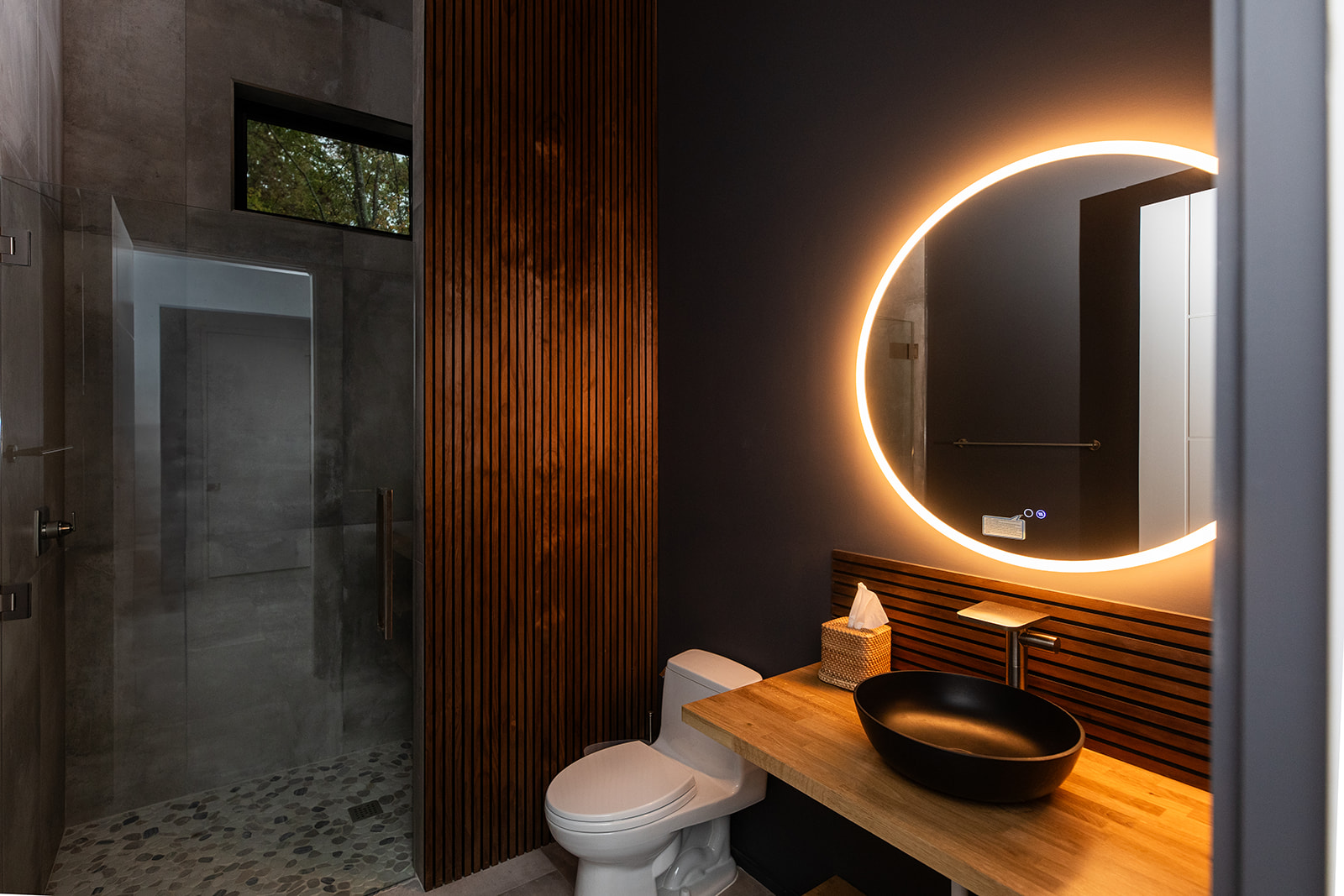 Modern bathroom with circle mirror backlight, wood detail, and vessel sink