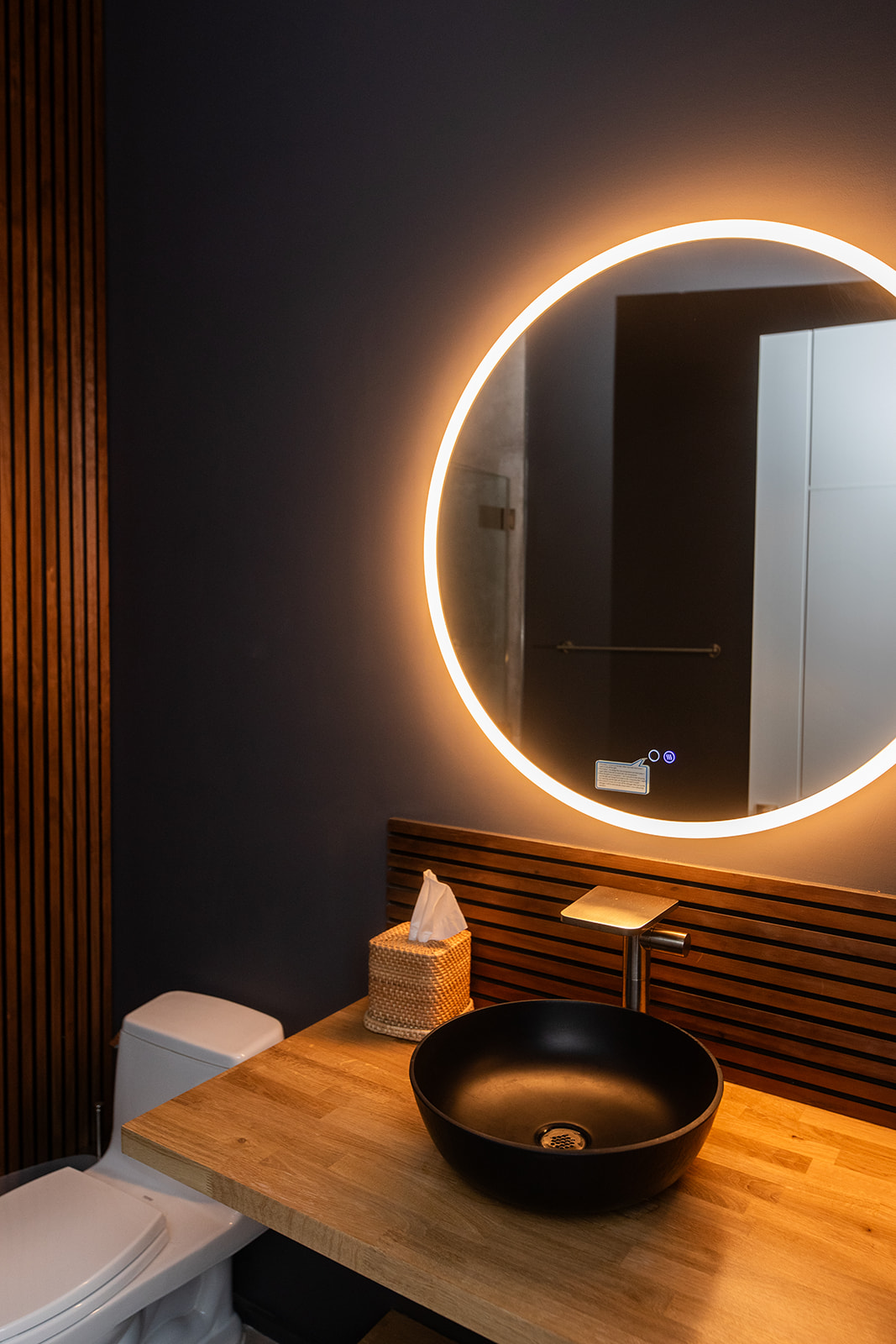 Modern bathroom with circle mirror backlight, wood detail, and vessel sink