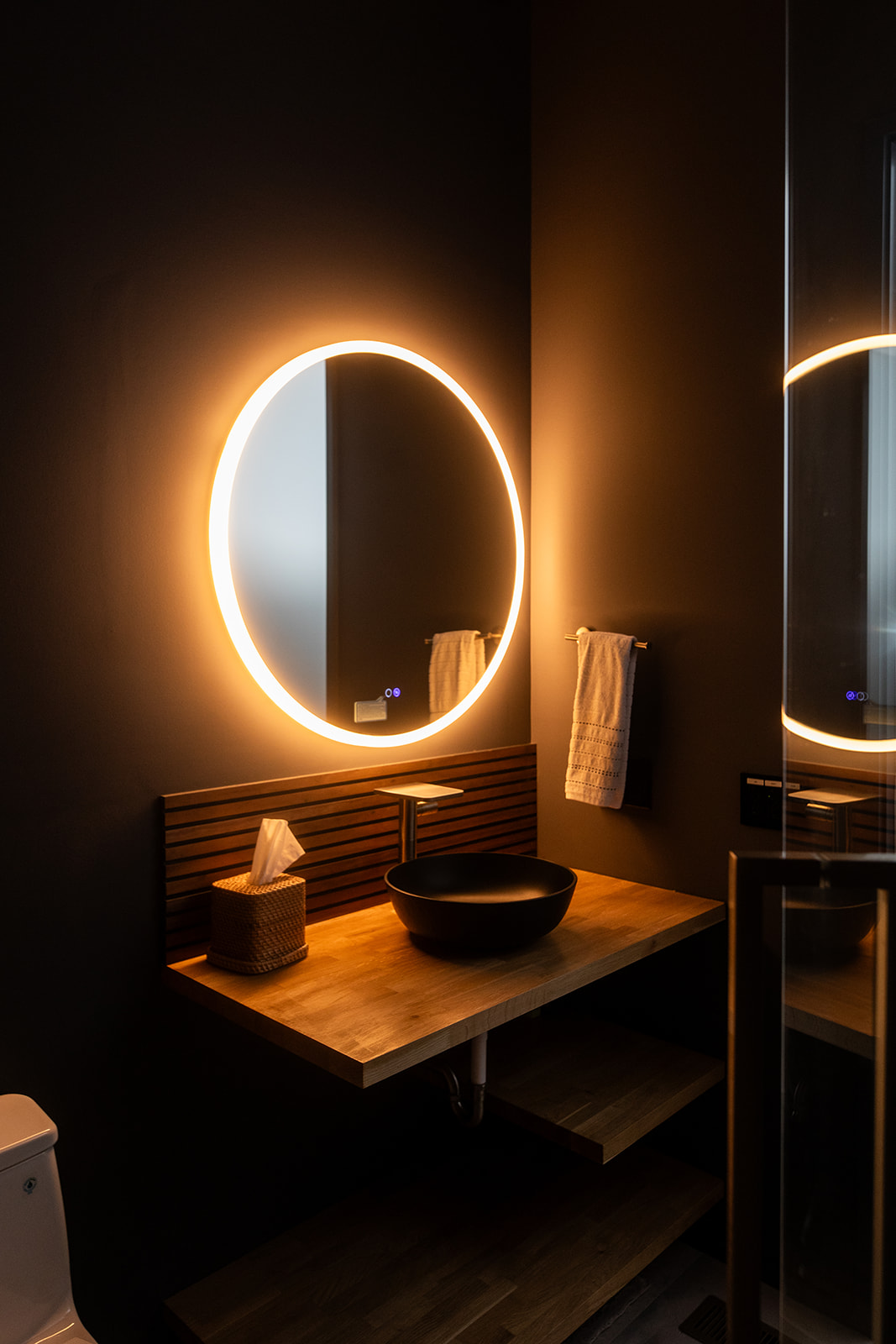 Modern bathroom with circle mirror backlight, wood detail, and vessel sink