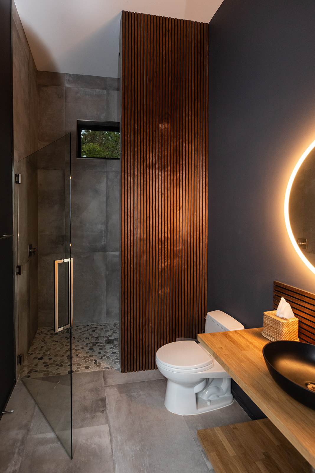 Modern gray bathroom with glass shower door and wood detail