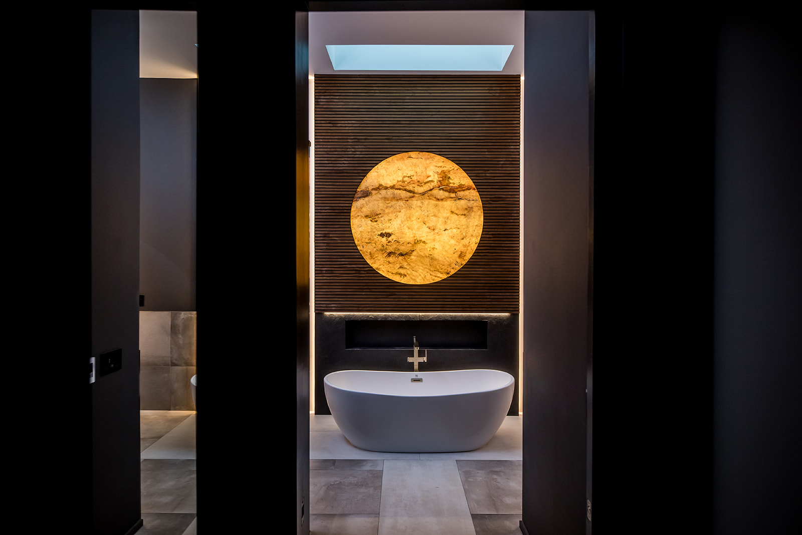 Modern bathroom with freestanding tub and wall marble stone sun moon and wood detail and backlit circle mirror