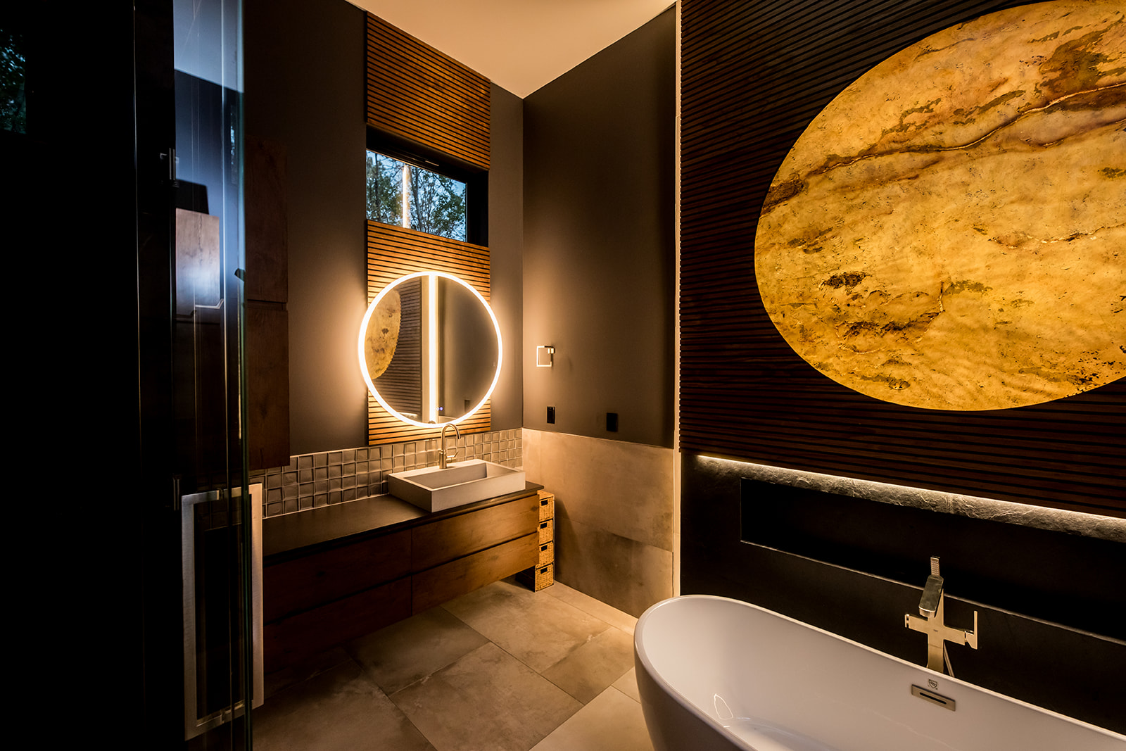 Modern bathroom with freestanding tub and wall marble stone sun moon and wood detail and backlit circle mirror