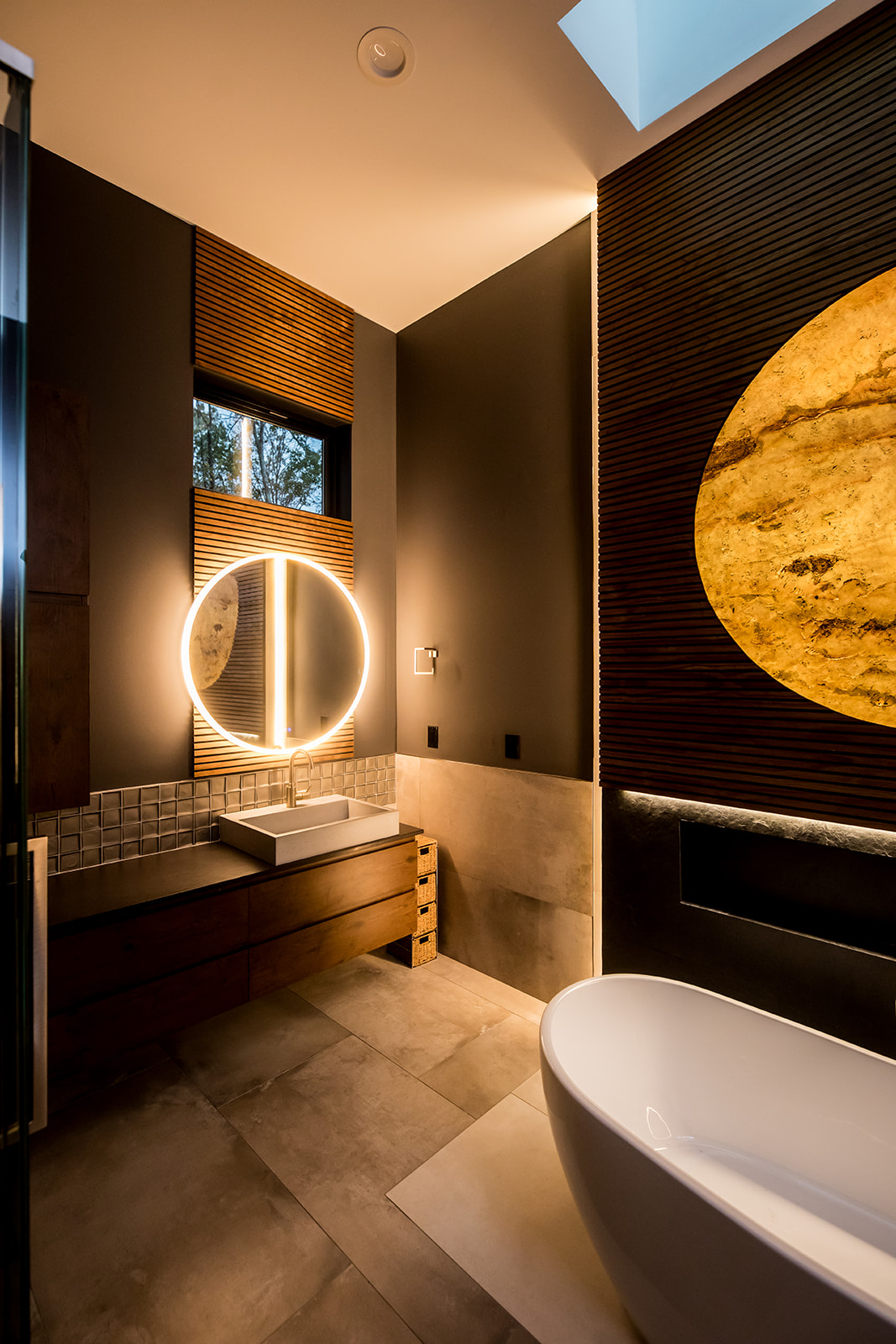 Modern bathroom with freestanding tub and wall marble stone sun moon and wood detail and backlit circle mirror