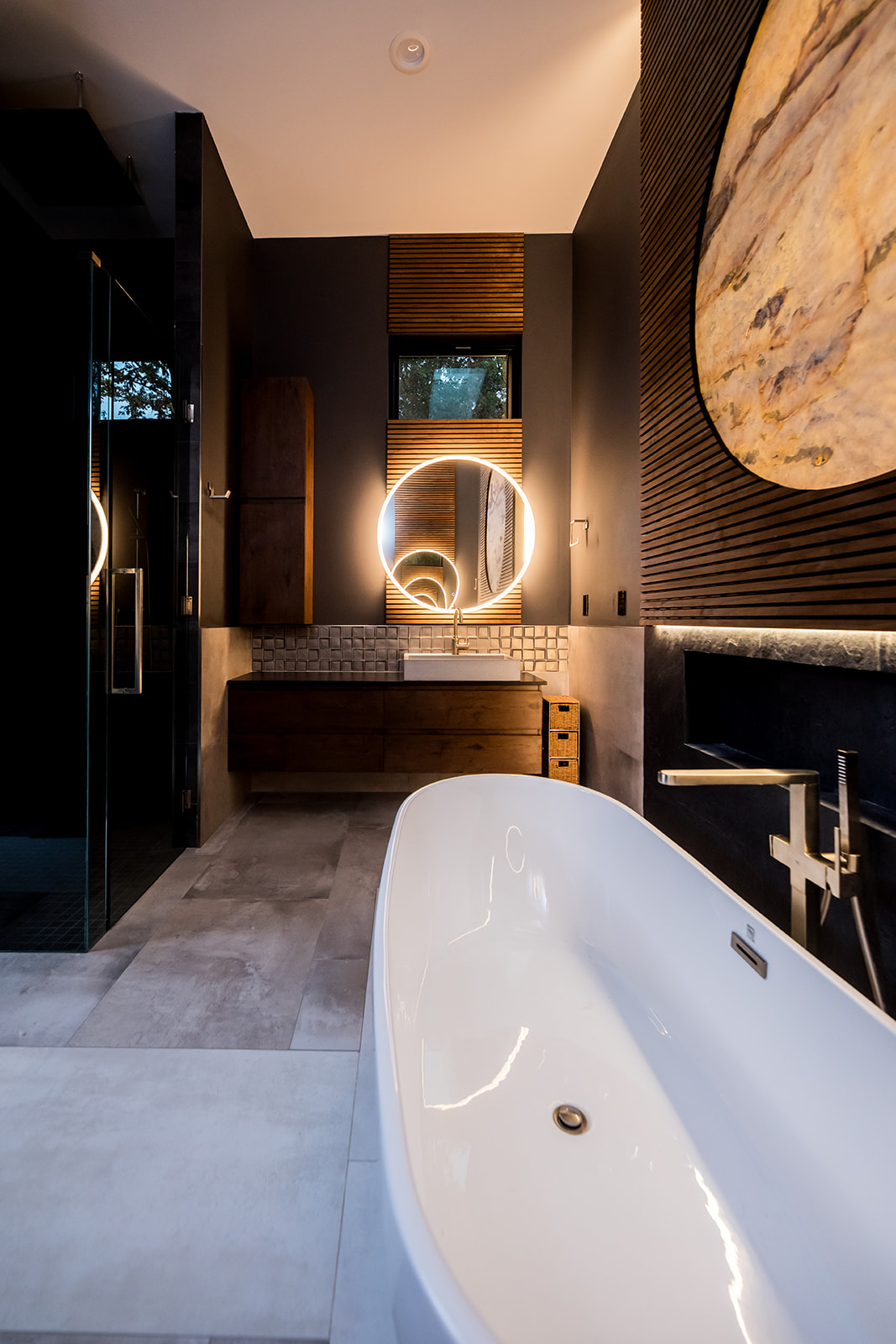 Modern bathroom with freestanding tub and wall marble stone sun moon and wood detail and backlit circle mirror