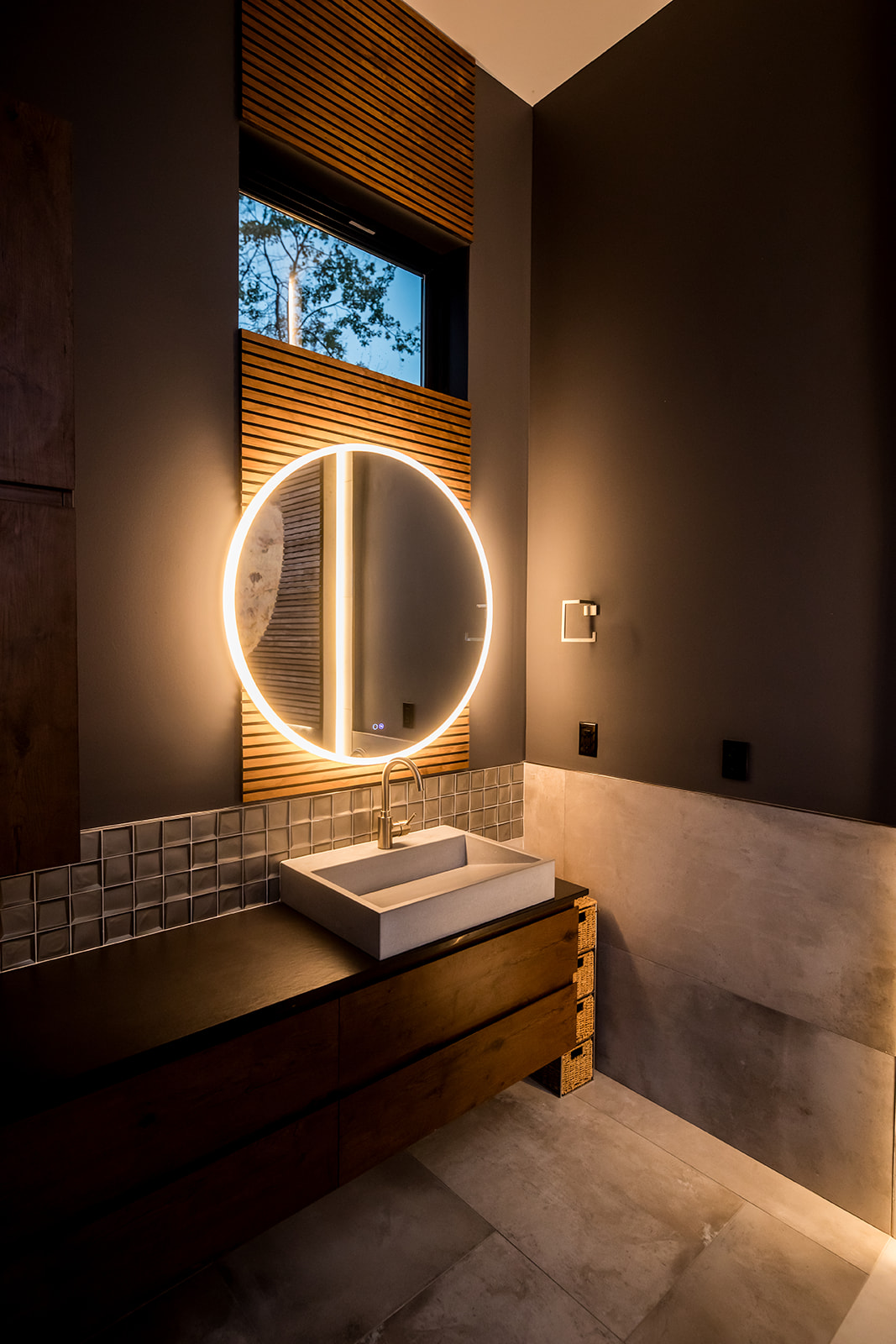 Modern bathroom with tile backsplash, wood detail, and circle mirror with backlight