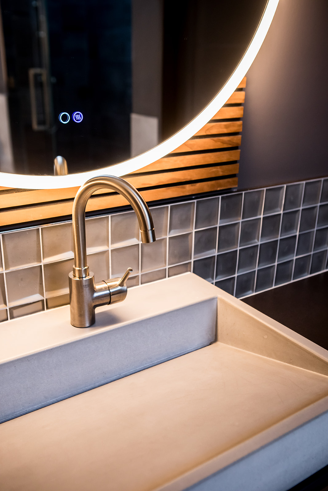 Modern bathroom with tile backsplash, wood detail, and circle smart mirror with backlight