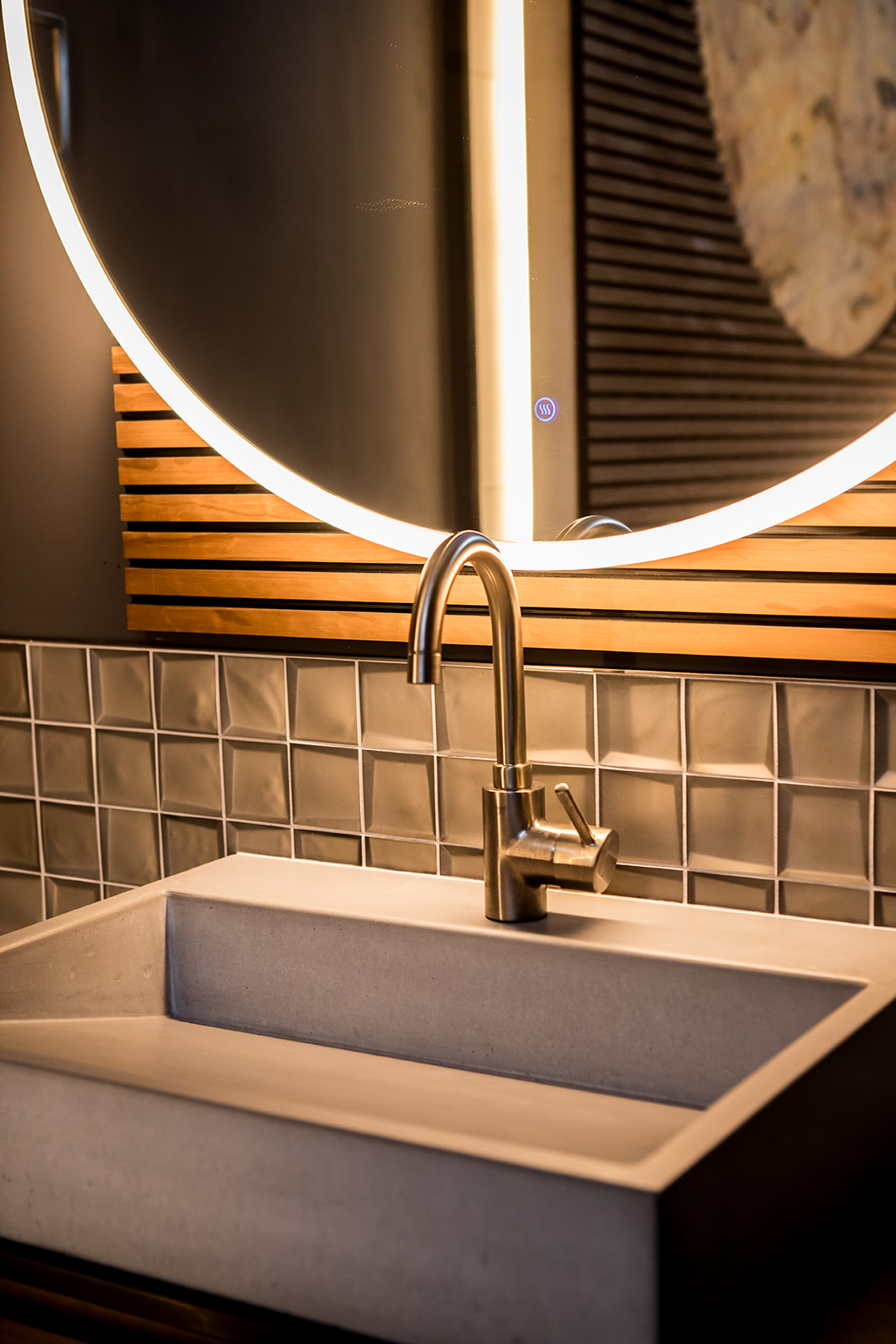 Modern bathroom with tile backsplash, wood detail, and circle mirror with backlight