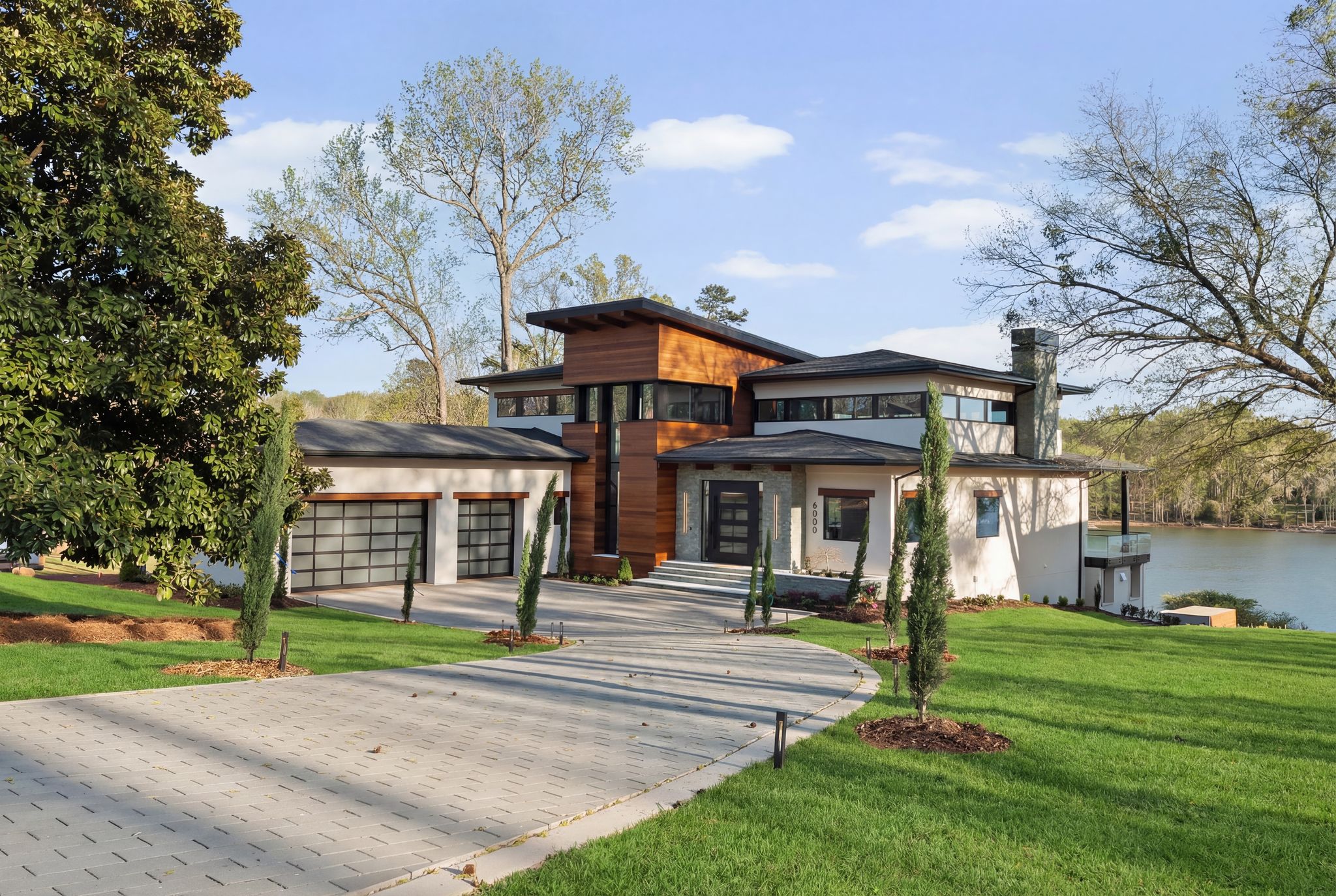 Modern lakefront home with wood and stucco facade, paver driveway and Lake Wylie beyond
