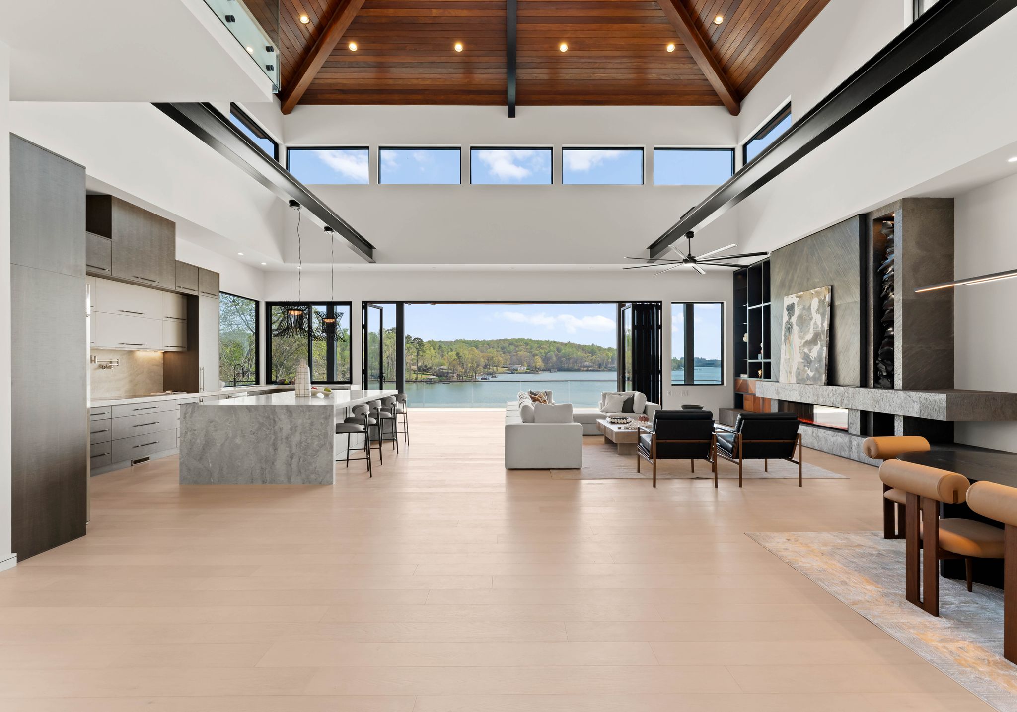 Great room with vaulted wood ceiling, clerestory windows, kitchen island and folding glass doors open to the lake