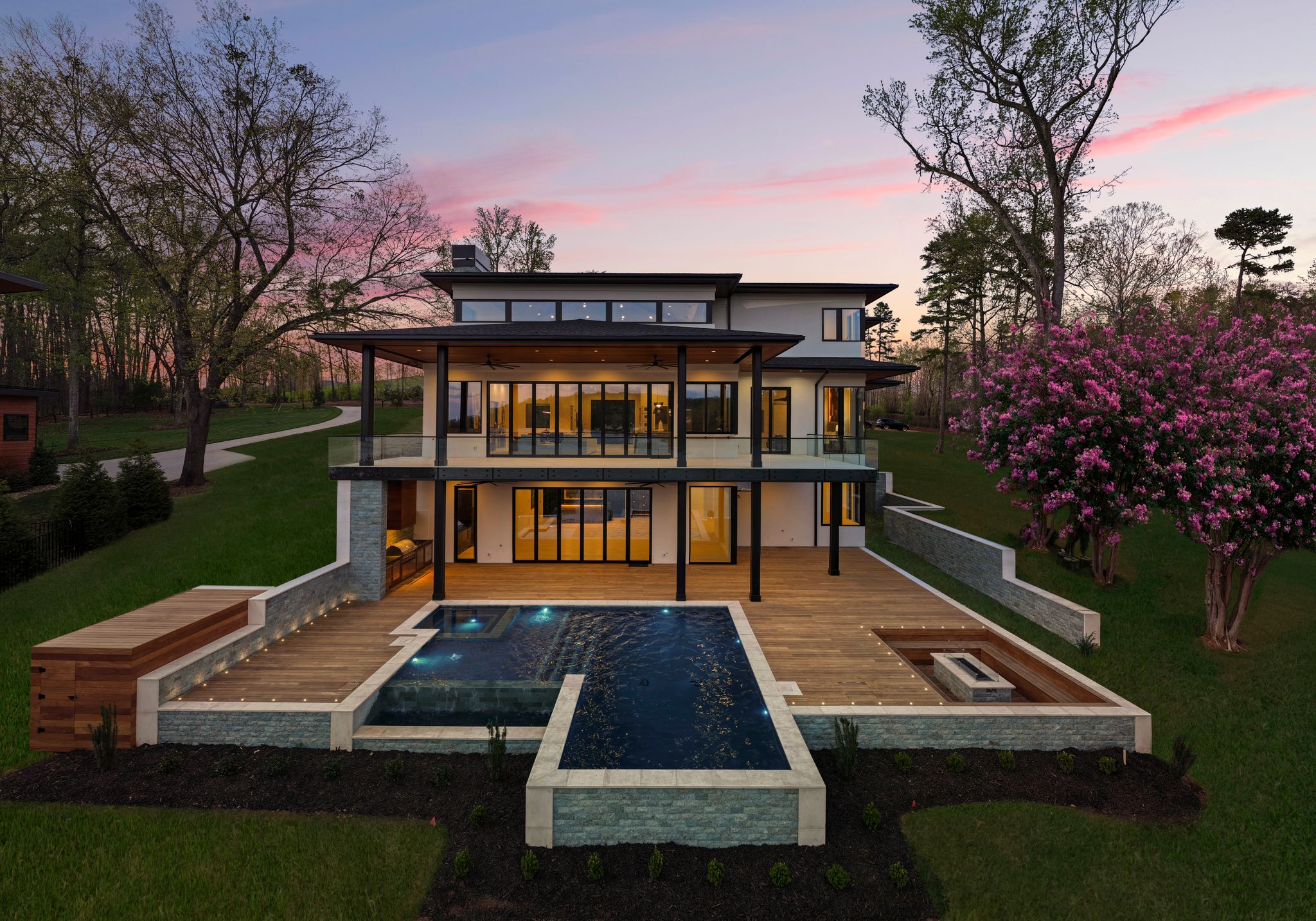Rear of a lakefront home at dusk with pool and spa, wood deck, fire pit and covered terraces